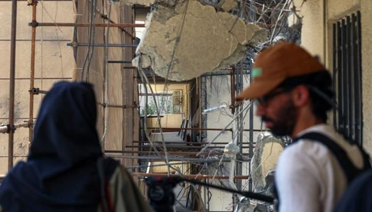 شاب وفتاة في إيران أمام مبنى متضرر جراء القصف الإسرائيلي