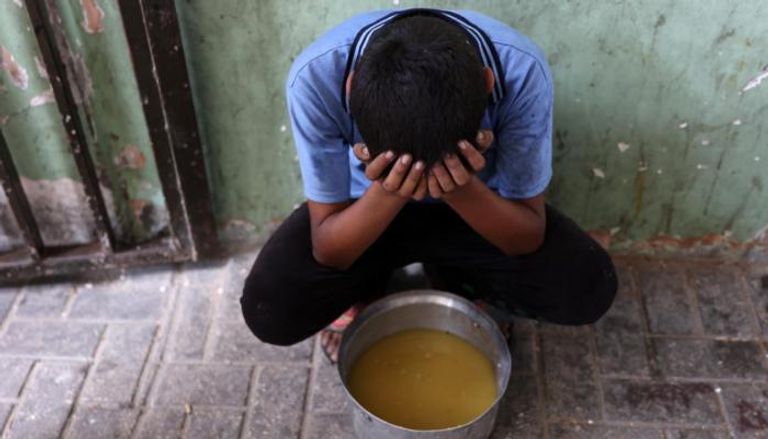 طفل فلسطيني نازح يجلس بجانب قدر من حساء العدس حصل عليه من مركز توزيع