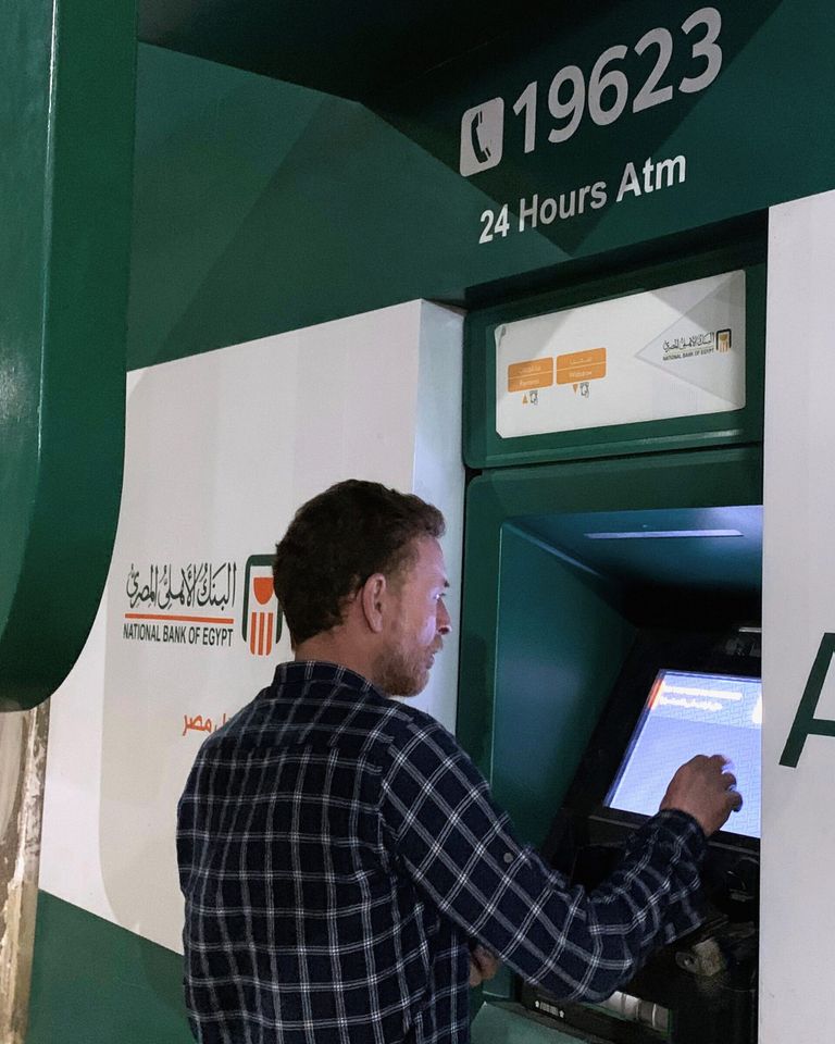 شخص سقف أمام ماكينة تابعة للبنك الأهلي المصري - رويترز