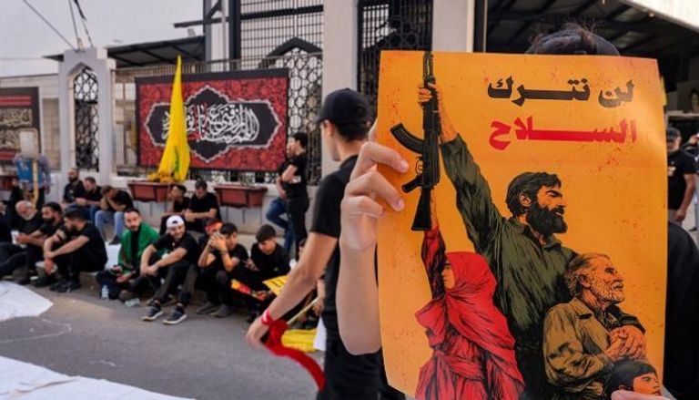 أحد عناصر حزب الله يحمل لافتة كُتب عليها «لن نتخلى عن السلاح»