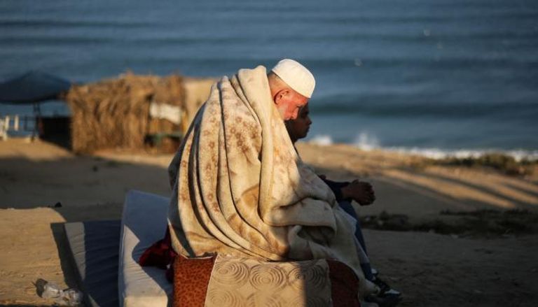 مسن فلسطيني وطفل يجلسان على شاطئ غزة