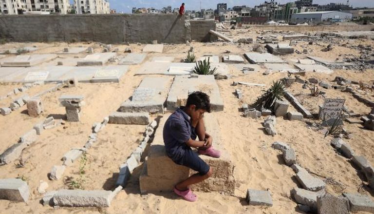طفل يجلس فوق قبر في خان يونس