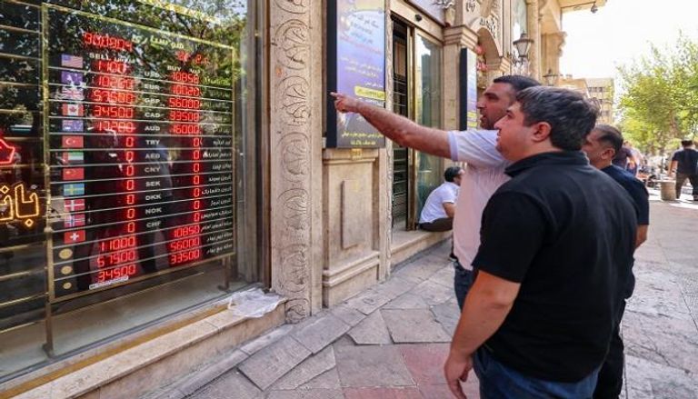 أشخاص يشاهدون أسعار صرف العملات المعروضة على واجهة متجر في طهران
