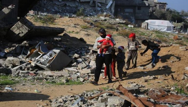 فلسطيني يسير مع أطفال بجوار أنقاض المباني المدمرة في مخيم جباليا للاجئين