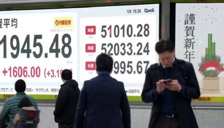 يابانيون يمرون أمام شاشة لعرض الأسهم في طوكيو