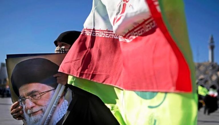 امرأة إيرانية تحمل العلم الوطني وصورة المرشد الإيراني علي خامنئي
