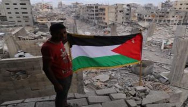 فلسطيني يحمل علم بلاده وسط أنقاض المنازل المدمرة في غزة