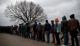 مهاجرون يصطفون للحصول على غذاء بأحد مخيمات اللاجئين على الحدود اليونانية المقدونية - رويترز