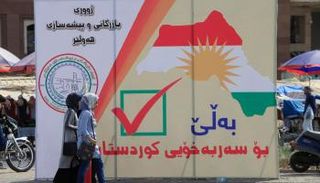 نساء عراقيات يمشين بجانب يافطة كردية للاستقلال بأربيل (رويترز)