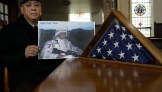 والد ميجيل  بيريز يمسك صورته حين كان في الجيش (الفرنسية)