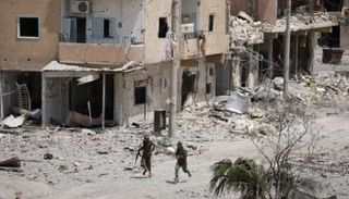 مقاتلان من قوات سوريا الديمقراطية يركضان وسط منازل مهدمة في الرقة