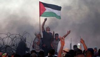 شبان فلسطينيون يحملون العلم قرب السياج الحدوي - رويترز