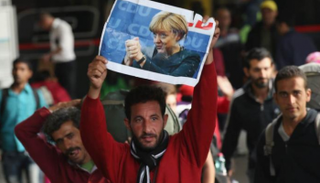 أحد اللاجئين يرفع صورة المستشارة الألمانية أنجيلا ميركل- أرشيفية