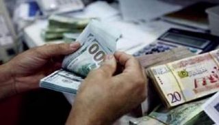 موظف يحصي أوراقًا من فئة الـ100 دولار في أحد مصارف ليبيا (أرشيفية)
