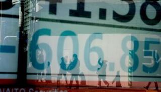 أحد المشاة يرتدي قناعا للوجه يمر عبر لوحة تعرض مؤشر نيكي 225 