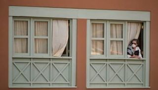 سيدة تضع كمامة وتنظر من نافذة منزلها