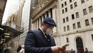 رجل يرتدي قناعًا وقائيًا أثناء سيره في وول ستريت 