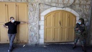 فلسطيني يرتدي الكمامة ينظر إلى جندي إسرائيلي في مدينة الخليل