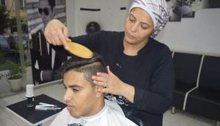 عبير مصطفى تصفف شعر أحد زبائنها في صالونها الخاص