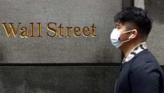 رجل يرتدي قناعا واقيا وهو يمشي بجوار وول ستريت