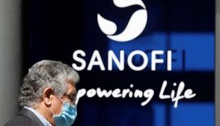 رجل يرتدي كمامة أمام شعار شركة "سانوفي"