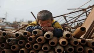 طفل سوري يجوار القذائف الفارغة