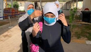 معلمة تساعد إحدى الطالبات في ارتداء الكمامة (أرشيفية)