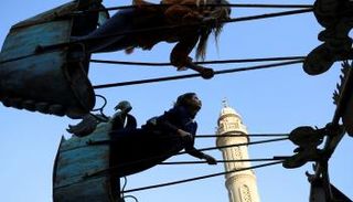 أطفال مصريون يلعبون بأحد الملاهي فيما تظهر في الخلفية مئذنة مسجد عمرو بن العاص في القاهرة
