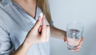 سيدة تمسك بعقار وكوب ماء قبل تناوله
