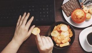 شخص يتناول المقرمشات وهو يعمل على الكمبيوتر
