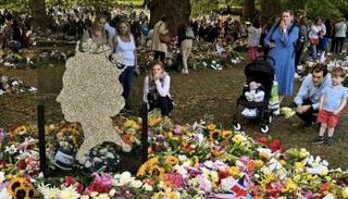 مواطنون ينظرون إلى باقات زهور ورسائل تكريما لروح الملكة