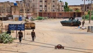 جنود الجيش السوداني يسيرون قرب عربات مدرعة متمركزة في أحد شوارع جنوب الخرطوم