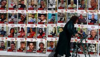 سيدة إسرائيلية تمر أمام حائط يحمل صورا لرهائن في غزة