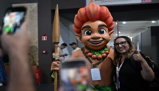 امرأة ترفع إبهامها أثناء التقاط صورة مع تميمة مؤتمر COP30 - أ ف ب