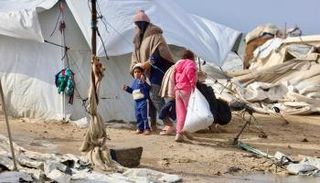 فلسطينية نازحة وطفلاها بجوار الخيام والملاجئ بغزة