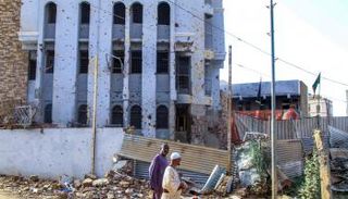 سودانيان يمران أمام مبنى مثقوب بالرصاص في أم درمان