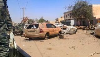 جندي بالجيش يلوح من خلف مركبة أثناء مرورها بجانب سيارات متضررة بالخرطوم