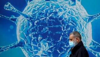 رجل يمر أمام صورة توضيحية لفيروس كورونا 