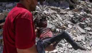 فلسطيني يحمل طفلة مصابة في قصف إسرائيلي بغزة