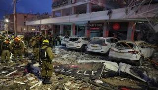 أفراد الطوارئ بجانب مبنى ومركبات متضررة بعد ضربة صاروخية إيرانية في إسرائيل