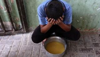 طفل فلسطيني نازح يجلس بجوار قدر من حساء في مدينة غزة