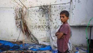 طفل فلسطيني بغزة بجوار حائط عليه آثار الرصاص - أ.ف.ب