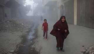 امرأة فلسطينية وأطفالها يهرعنَ بعيدًا عن موقع غارات شمال غزة