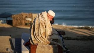 مسن فلسطيني وطفل يجلسان على شاطئ غزة