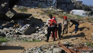 فلسطيني يسير مع أطفال بجوار أنقاض المباني المدمرة في مخيم جباليا للاجئين