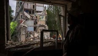 أحد سكان كييف ينظر من نافذة مبنى مدمر