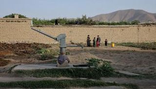 أطفال يقفون بالقرب من مضخة مياه يدوية جافة وسط أزمة مياه في كابول (رويترز)