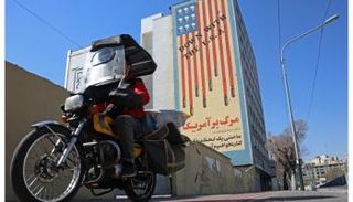 رجل إيراني يمر بدراجته أمام جدارية مناهضة لأمريكا على مبنى بطهران