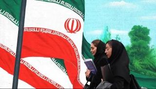إيرانيتان تمران أمام جدارية لأعلام إيرانية في طهران