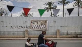 رجل يقود دراجة كهربائية يمر أمام لافتة حملة انتخابية تعرض مرشحين لمحافظة أريحا 